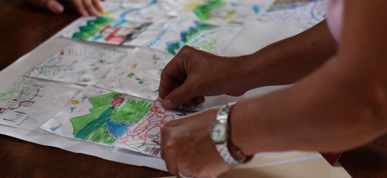 Manos de mujer colocando su dibujo hecho a mano en la mesa al lado de otros dibujos de montañas y ríos.